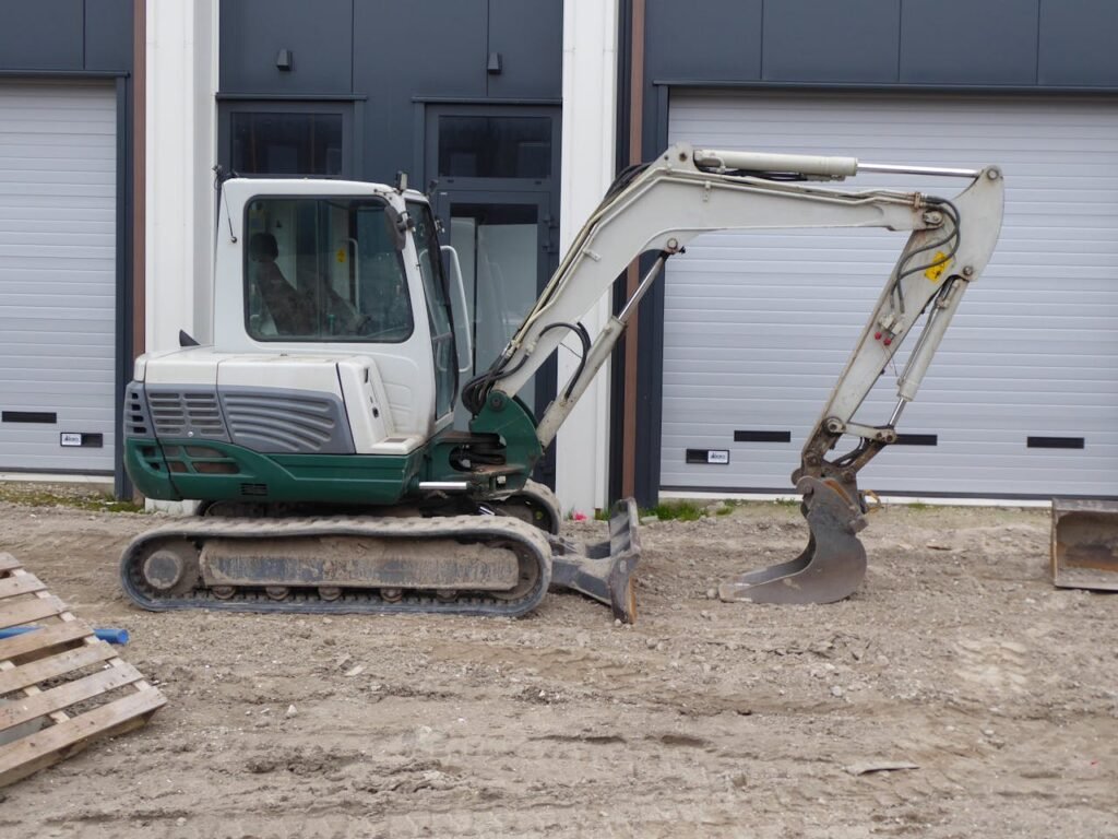Side view of a compact excavator on a construction site in front of a building.