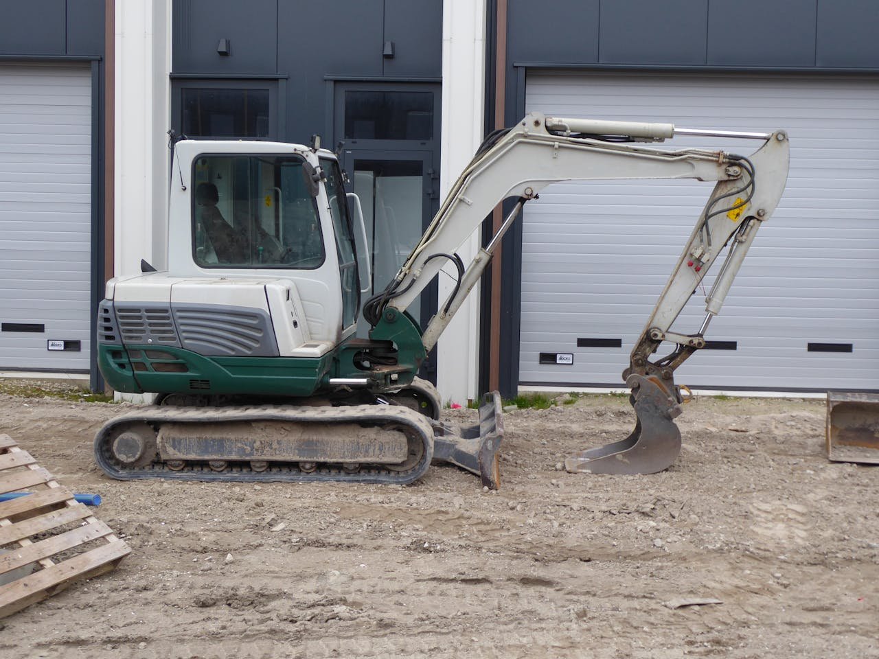 Side view of a compact excavator on a construction site in front of a building.