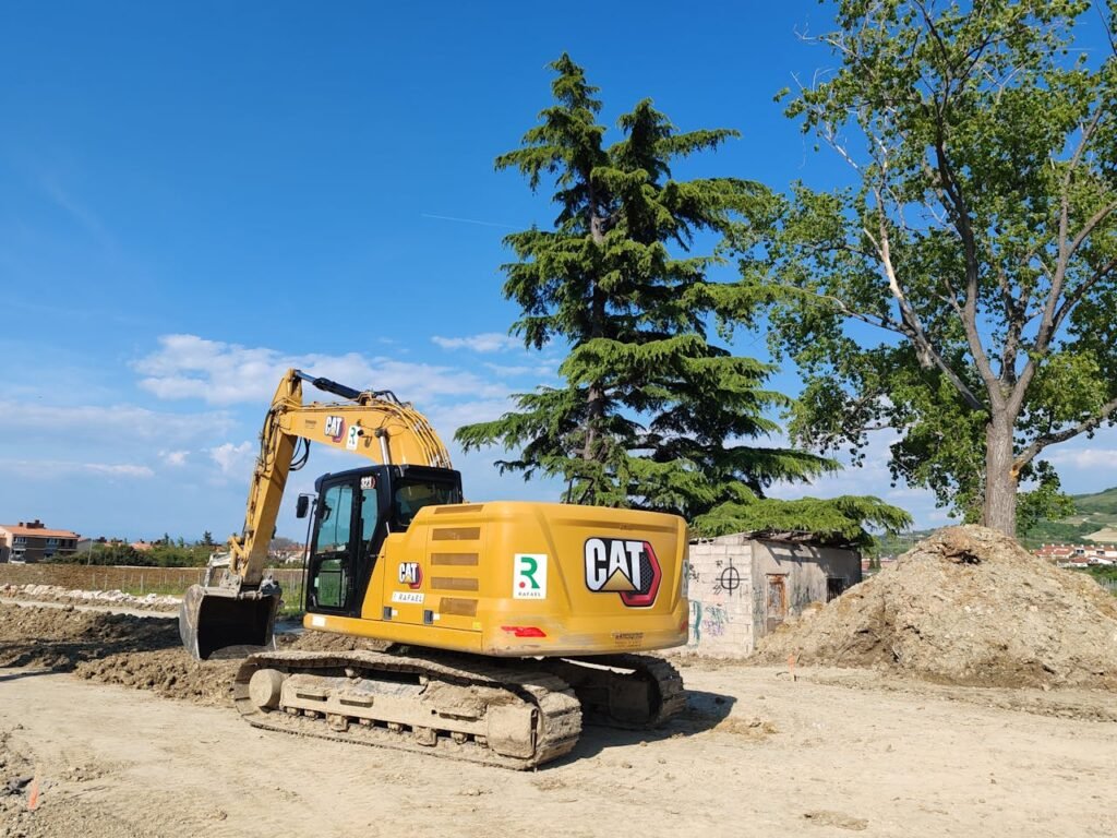 A CAT excavator working at a construction site with trees and blue sky in the background.